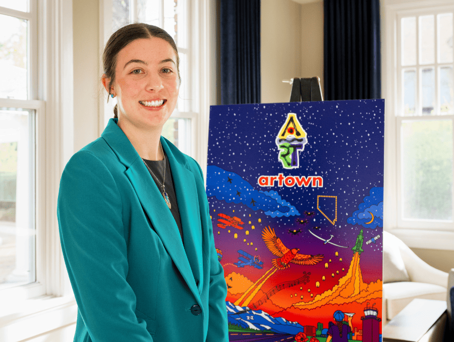 Reilly Moss stands in front of her mural chosen by Artown which depicts a sunset with planes, birds and other elements of Nevada.