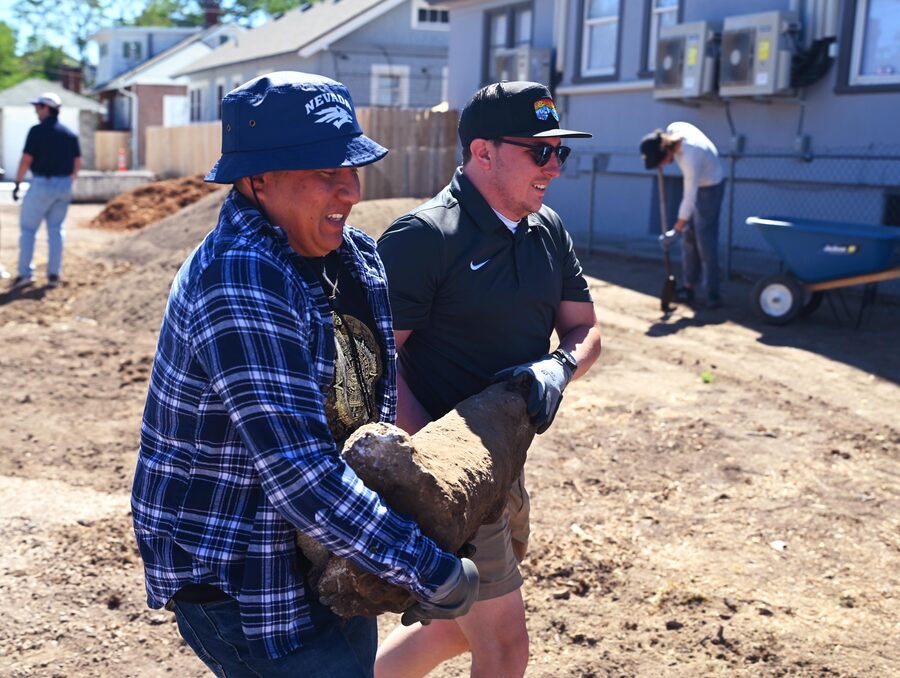 Two men carrying a heavy rock on a construction site.