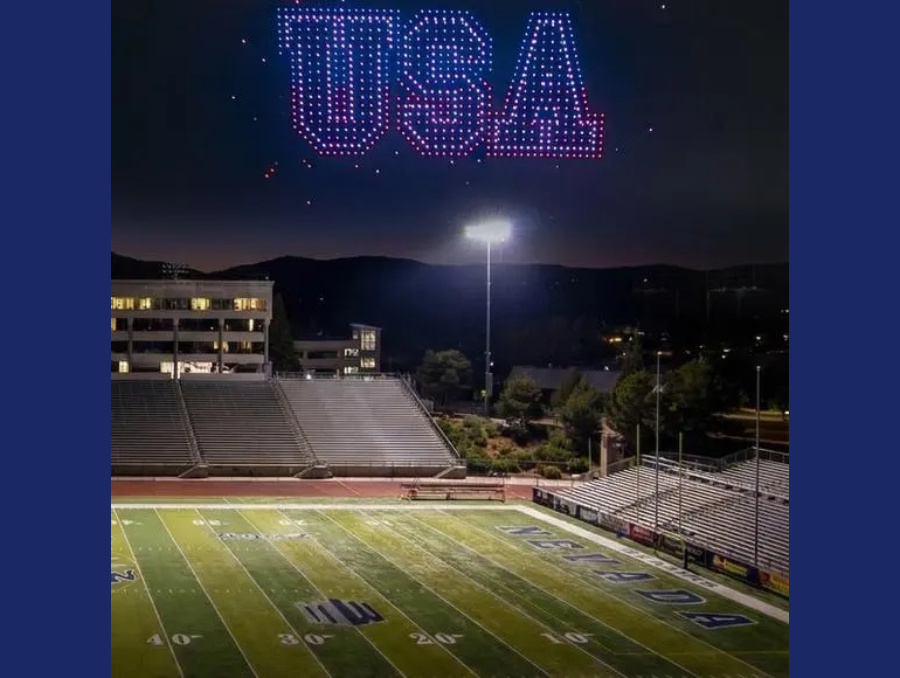 Mackay Stadium at night, with the lights on, and a large drone display in red, white, and blue spelling out "USA."