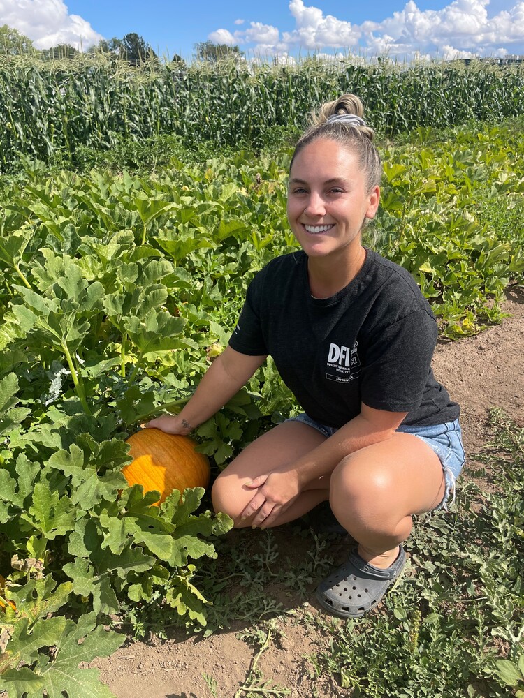 Monica Mori squatting  while holding a pumpkin in a pumpkin farm. 