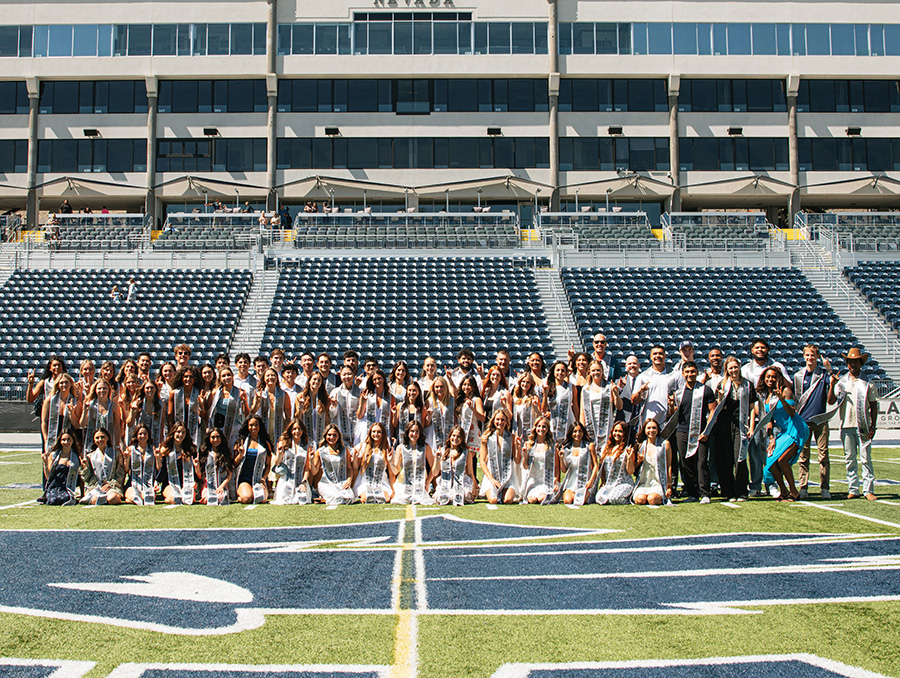 A large group of students with graduation stoles posing for a photo on Chris Ault Field.