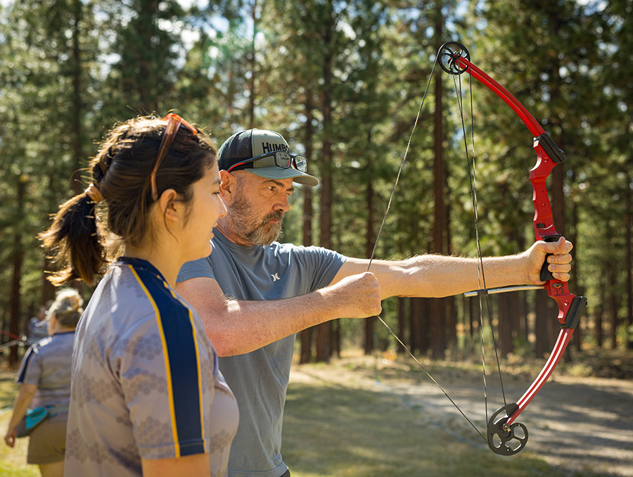 Chloe Yocom assists Karl with his bow and arrow.