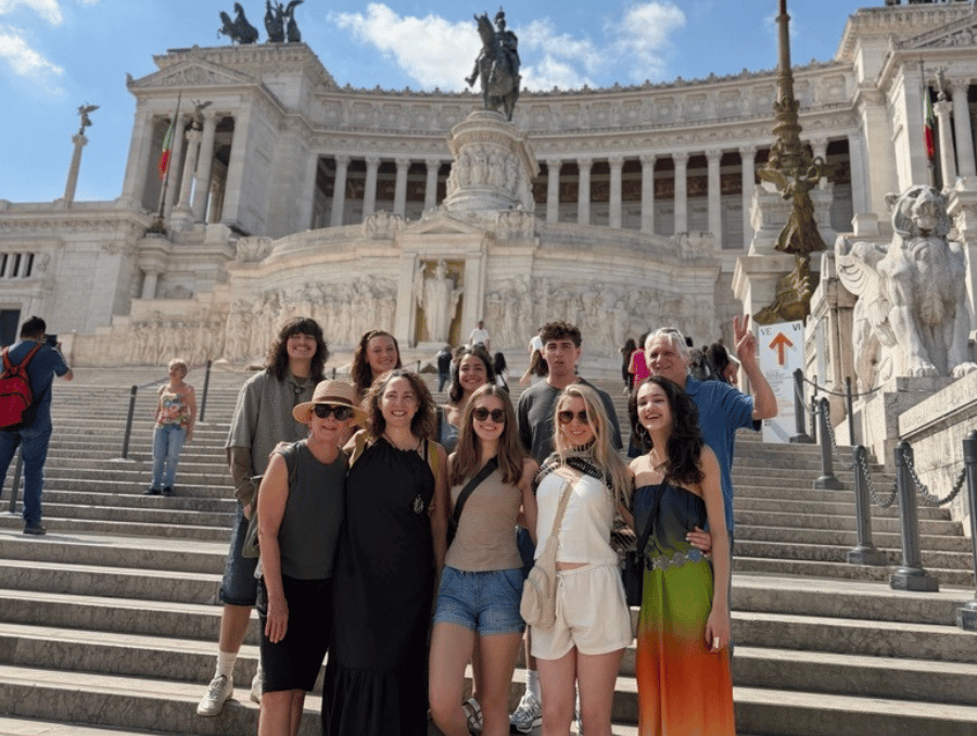 A group of students and the group leaders standing in front of Roman artifacts.