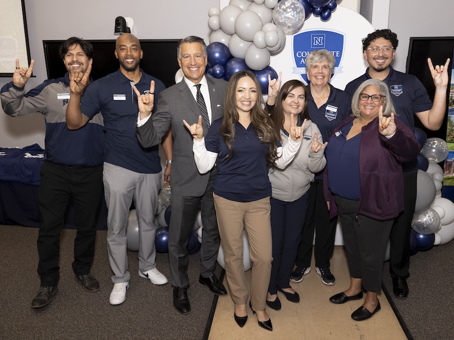 A group of University faculty, staff and leadership, including President Sandoval, pose smiling and holding up Wolf Pack hand signs.