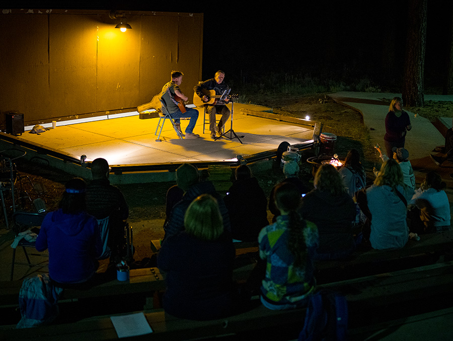 Doc Vaughn and Kjell Phillips playing guitar at night in front of a campfire.