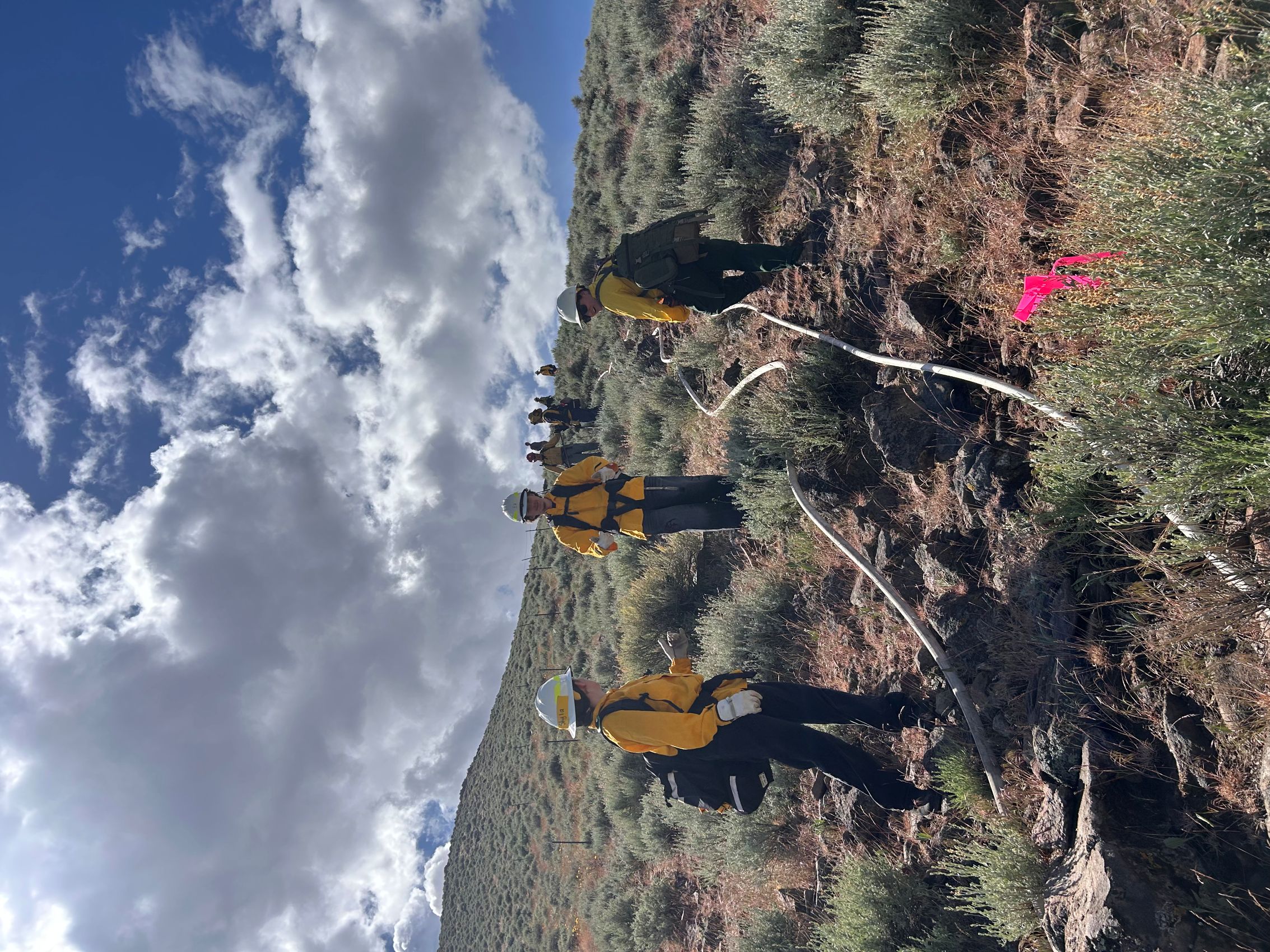 Firefighting students reeling a hose up a hill.