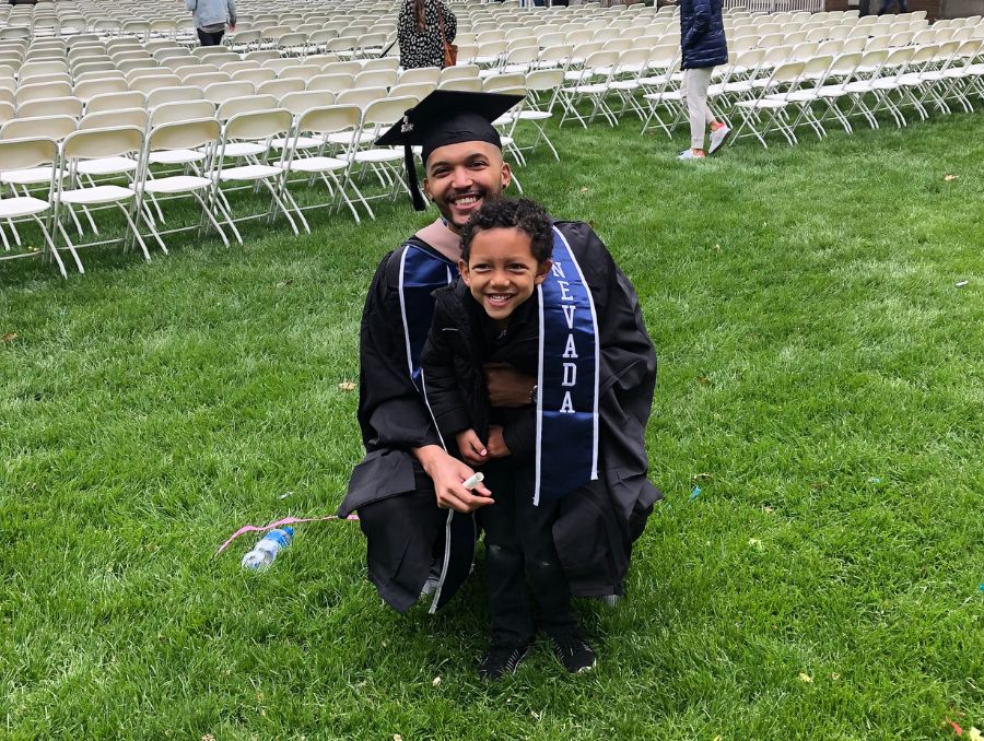 Brandon Ford in commencement cap and gown during a commencement ceremony, posing with his smiling son,Carter.