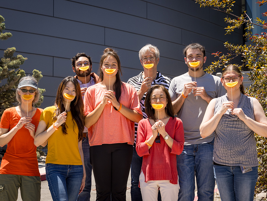 Members of the Jones Lab dressed in orange holding up orange slices in front of their faces in the shape of smiles.