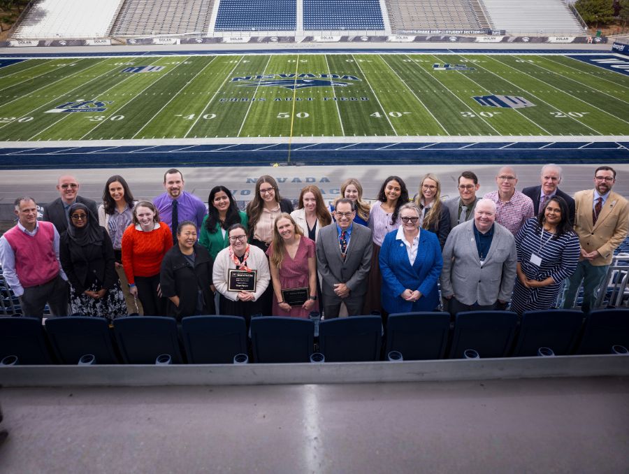 A group of students and faculty at the Mackay Stadium, smiling at the camera.