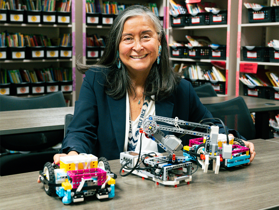 Rachel Salas, Ph.D. sits and poses with three Lego robots.