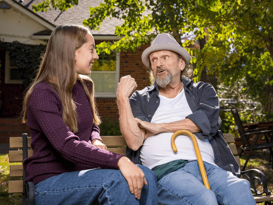 A younger woman sits in a bench with an older man outside.