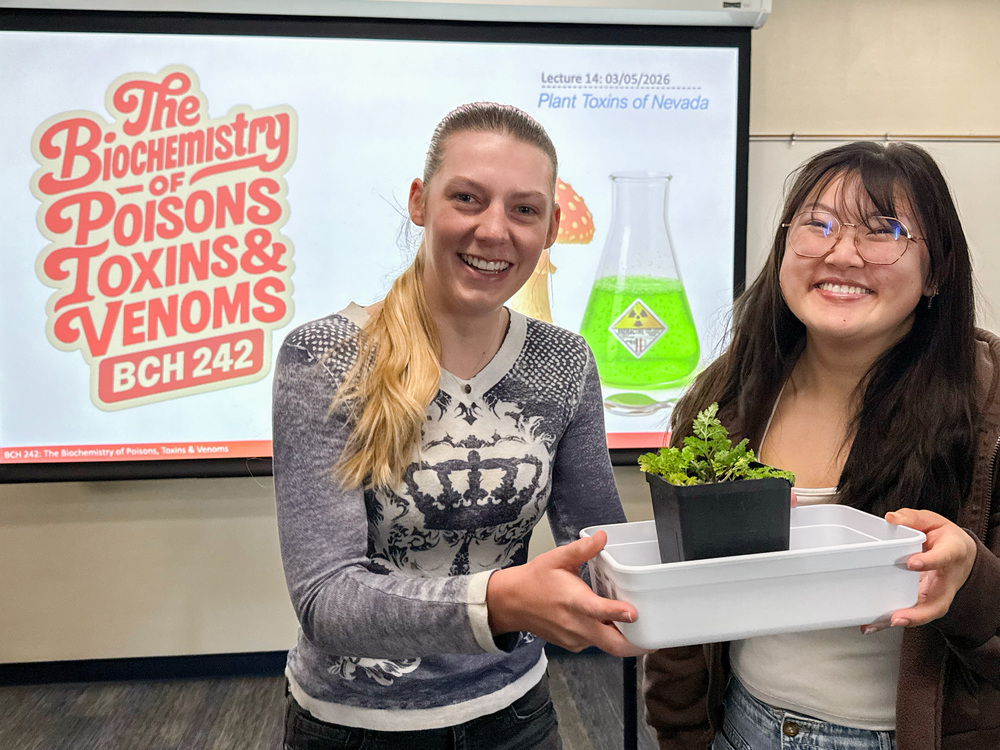 Two students holding a tray with a poisonous plant.
