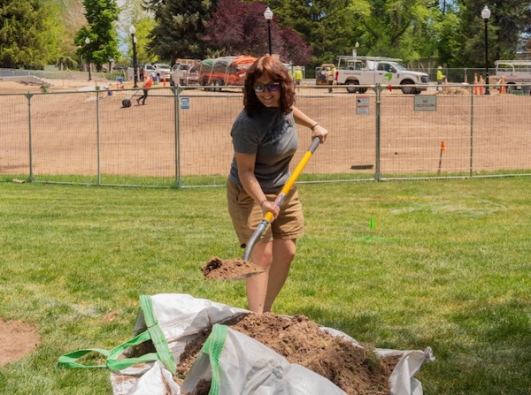 A woman holding a shovel, smiling, moves dirt from a large pile.