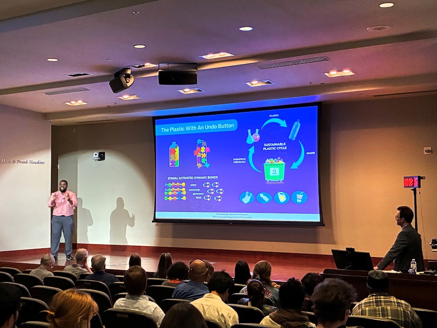 A man presenting a powerpoint presentation on stage. The slide reads "The plastic with an undo button" and shows graphics related to recycling.