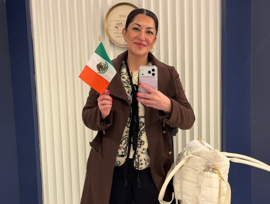 Vania at the airport with luggage and a small Mexican flag, smiling.