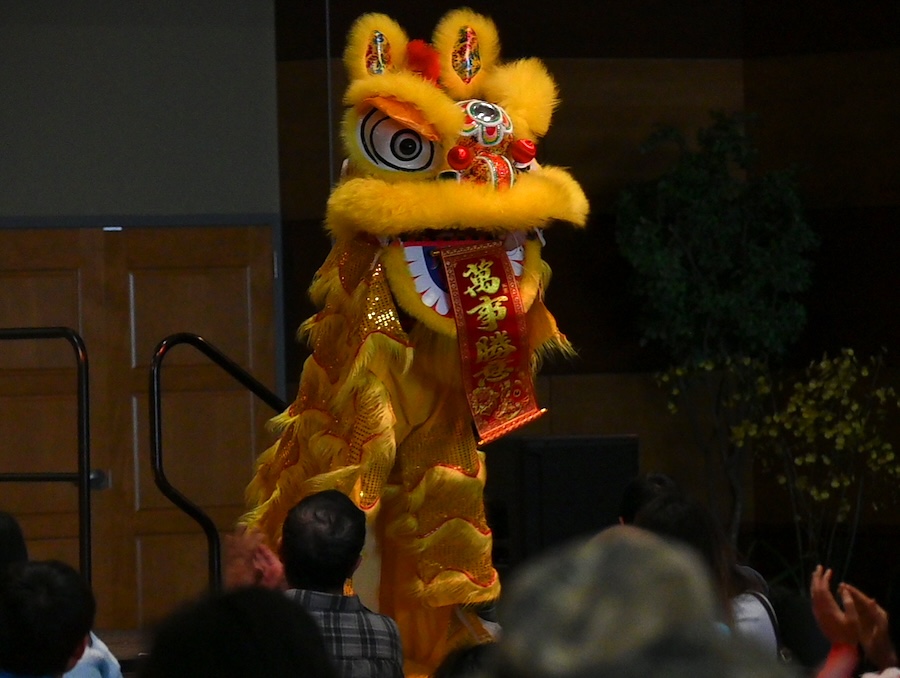 A troupe dancing in a yellow dragon costume on stage.