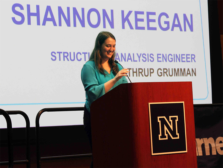 Woman stands at a podium, smiling; behind her is a screen that reads "Shannon Keegan, structural analysis engineering, Northrup Grumman."