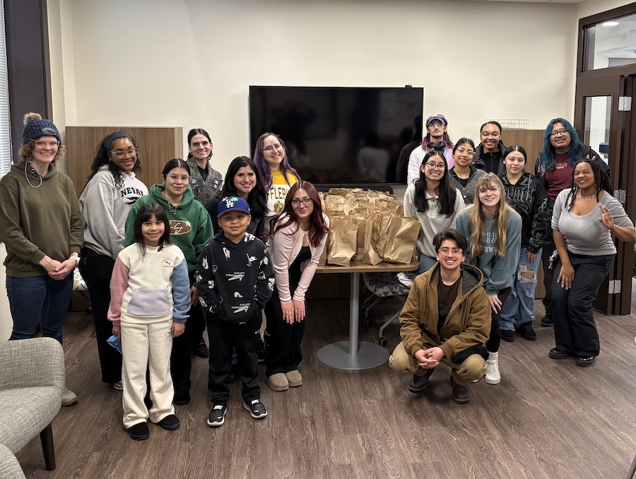 A group of about twenty people, including students and some younger kids, posing, smiling with housing kits in brown paper bags.