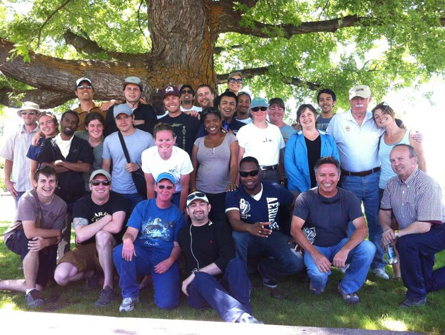 A group of 29 people smile for a photo under a shady, leafy tree.