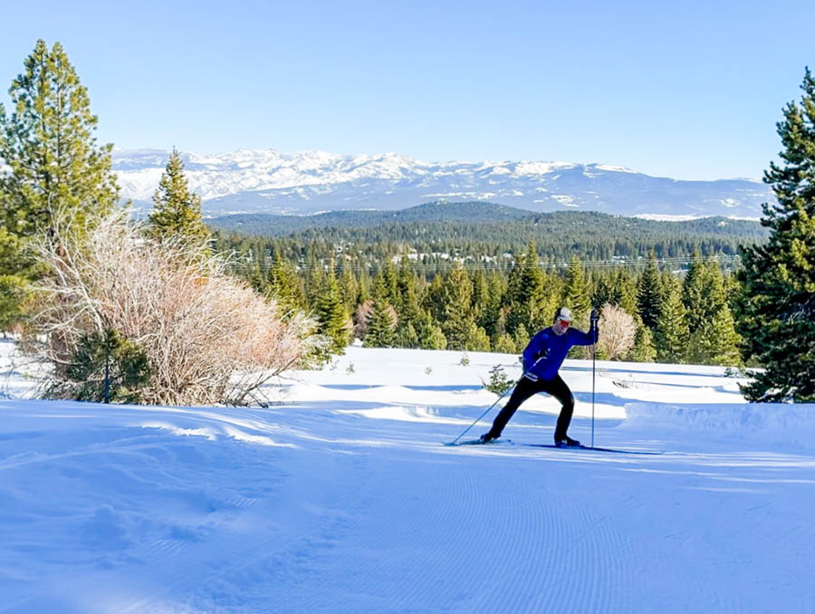 A cross country skier skis uphill with snowy mountains in the background.