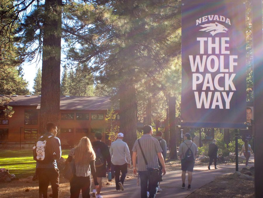 Students walk along a wooded path at the University of Nevada, Reno at Lake Tahoe campus, passing a banner that reads &ldquo;The Wolf Pack Way."