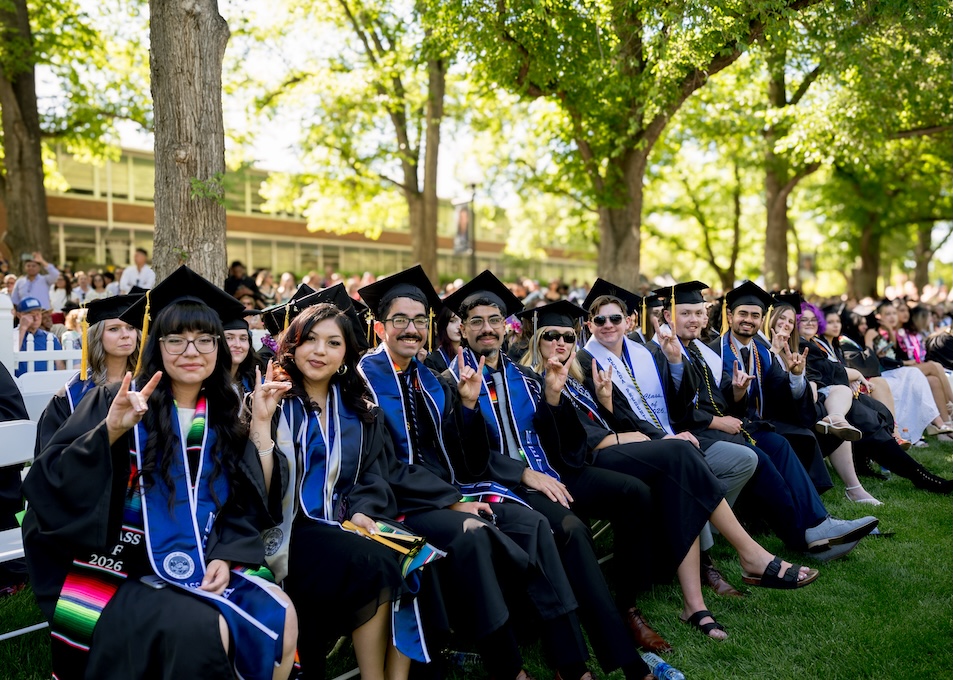 Group of graduates in caps and gowns on the quad, seated, smiling.