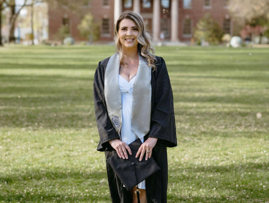 Dana Cooper dressed in graduation attire standing on University Quad