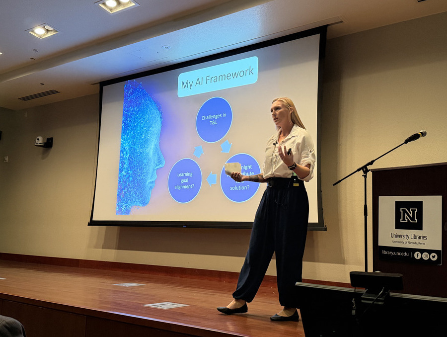 Professor stands on stage with slide about AI in background.