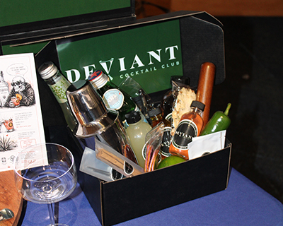 Open Deviant Cocktail Club kit box displaying cocktail ingredients, bar tools and recipe materials arranged inside.