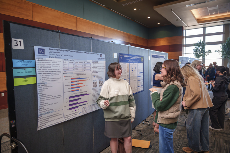 Student in front of a research poster speaking to an attendee. 