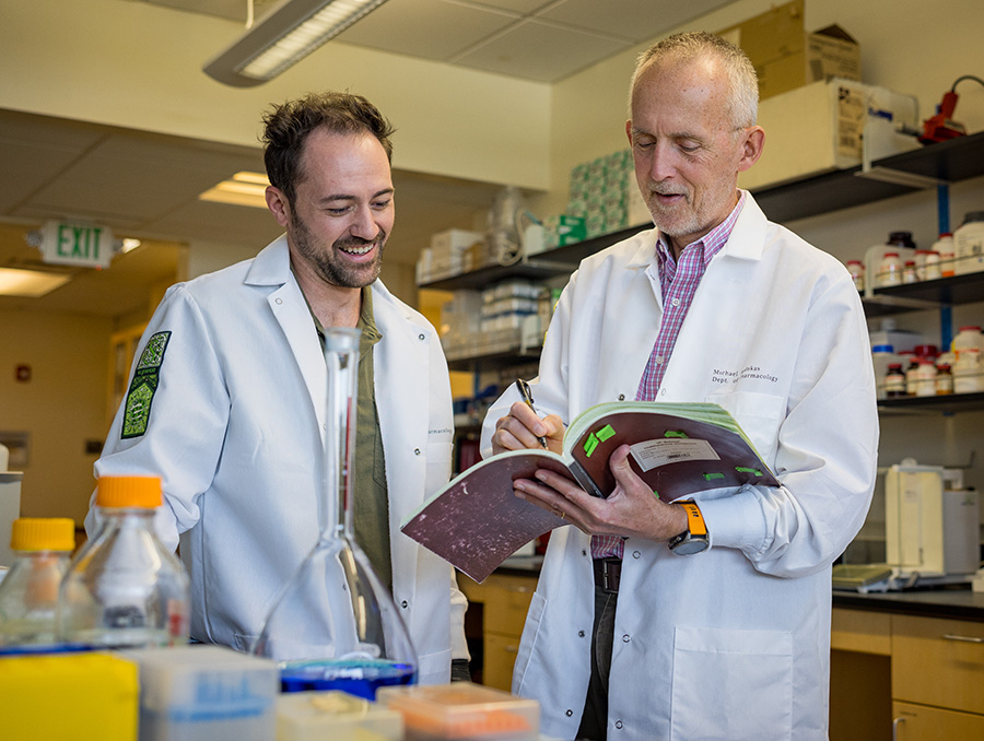 Robert Harvey, Ph.D., and postdoc Chase Fiore, Ph.D., looking at research findings in a notebook.