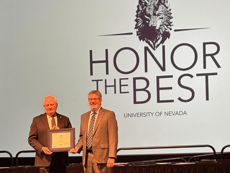 Peter Reed with the provost holding a certificate. Honor the Best signage is on the wall behind them.