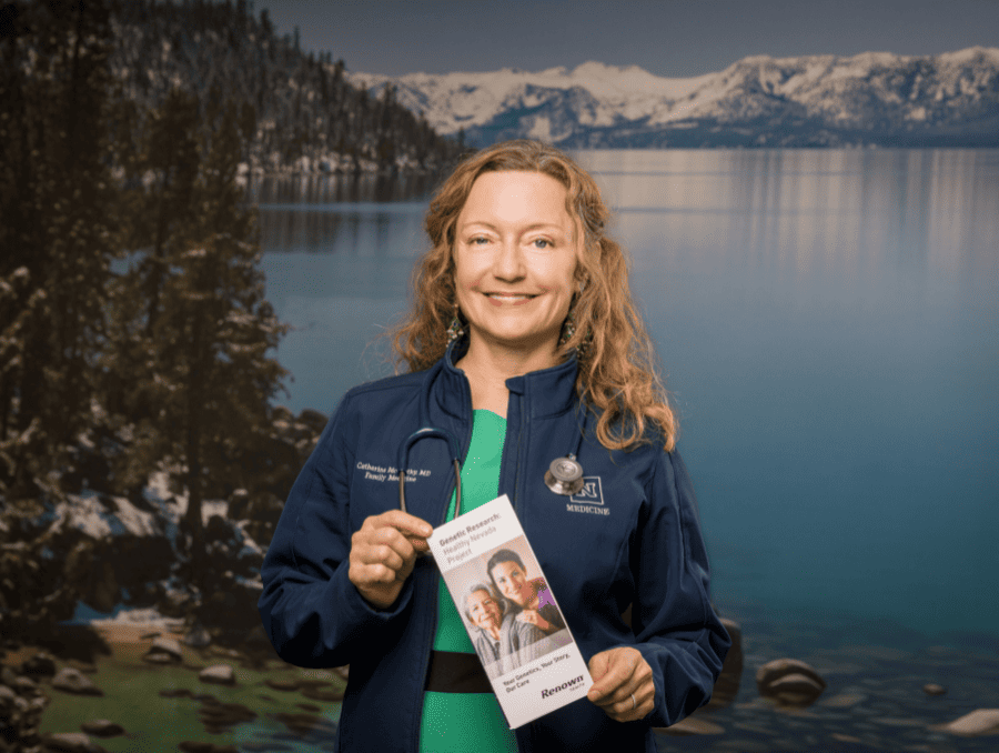 A woman wearing a stethescope, holding a brochure and standing in front of a mural of Lake Tahoe.