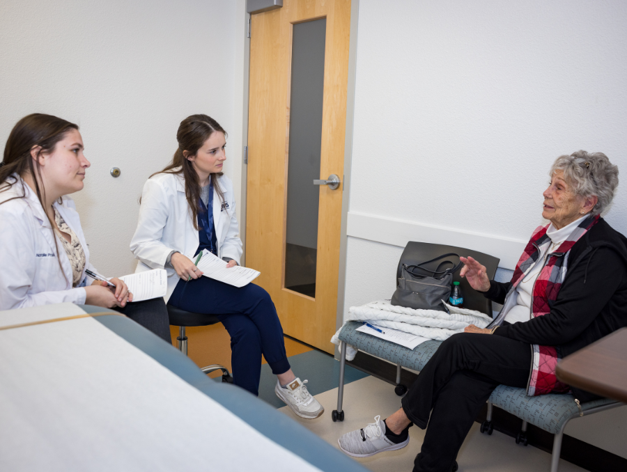 Two medical students meeting with an older adult in a clinic setting.