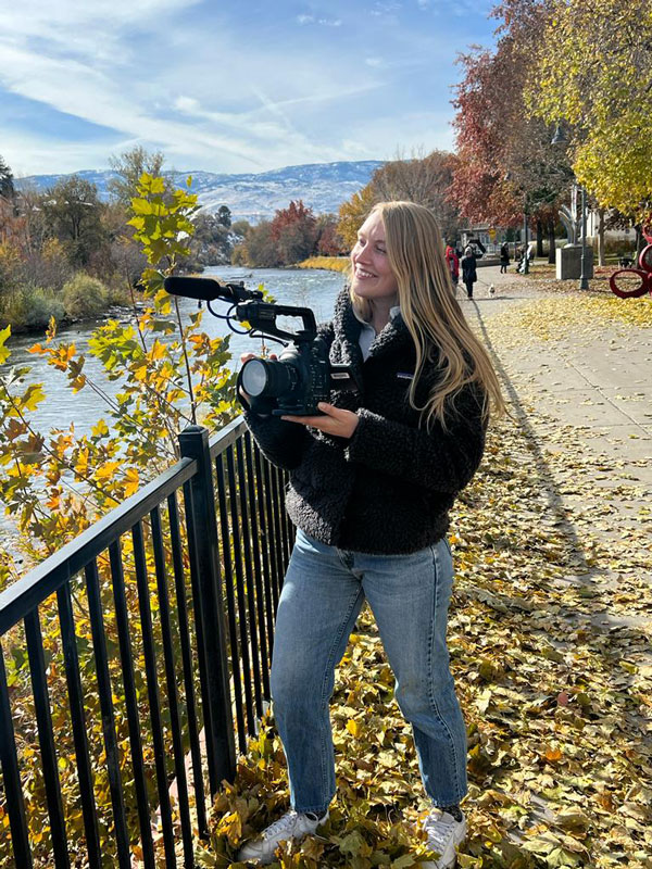Alex standing by the river holding a professional camera.