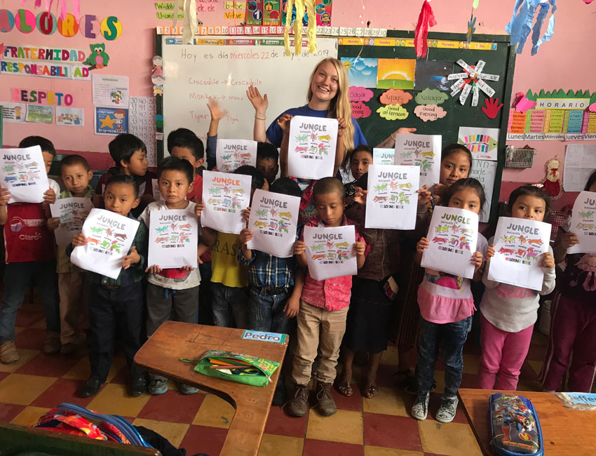 A group of children and Alex Couraud in a classroom holding up their artwork.