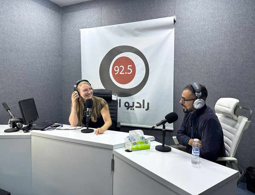 Two people sitting at a desk in a radio station studio. 