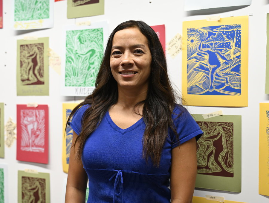 Ipuna Black, smiling, in front of a wall of artwork.