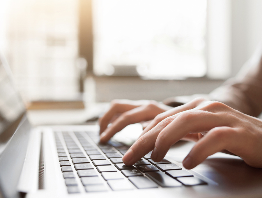 Close-up of hands typing on a laptop keyboard in a bright indoor workspace.