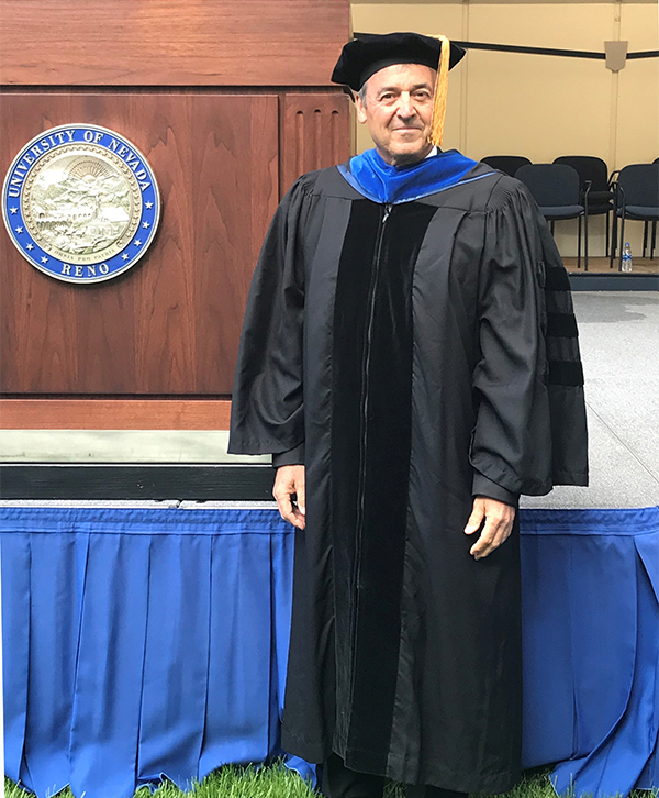 Ceccarelli in graduation gown and cap stands before a podium that read "University of Nevada, Reno."