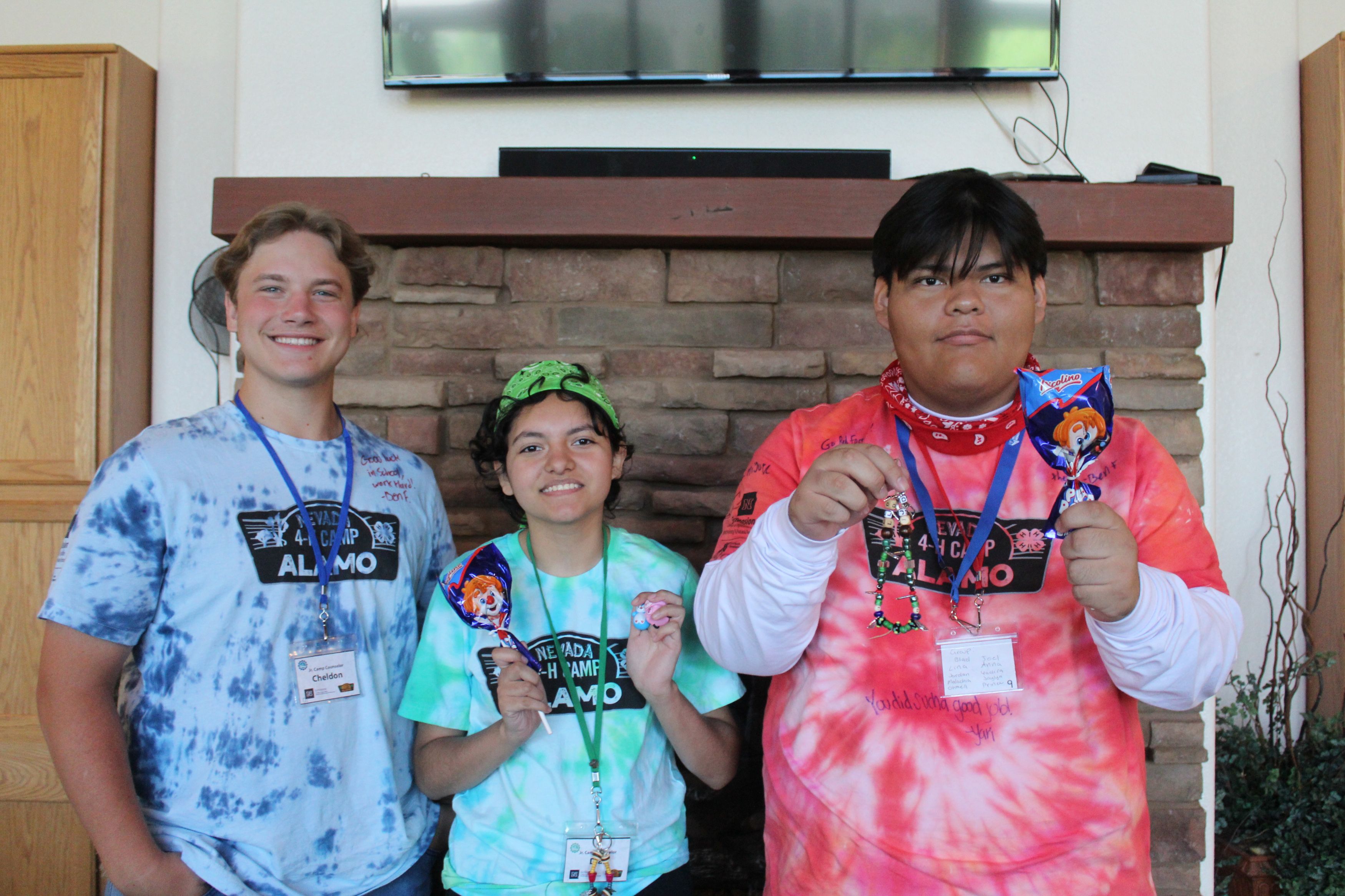 Cheldon posing with two other youth. They hold prizes and smile, wearing name badges and branded camp t-shirts.
