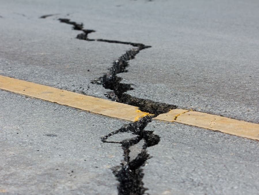 A road with a large crack down it, caused by an earthquake.