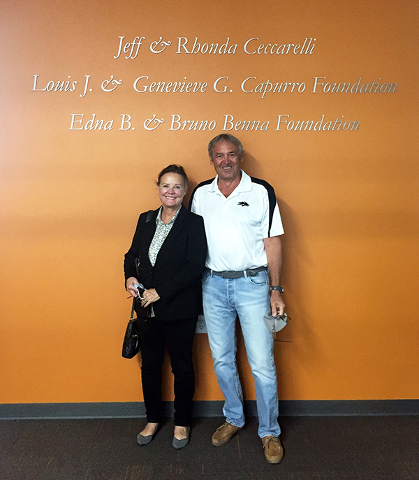 A woman and man stand against an orange wall under the words "Jeff & Rhonda Ceccarelli, Louis J. & Genevieve G. Capurro Foundation, Edna B. & Bruno Benna Foundation." 