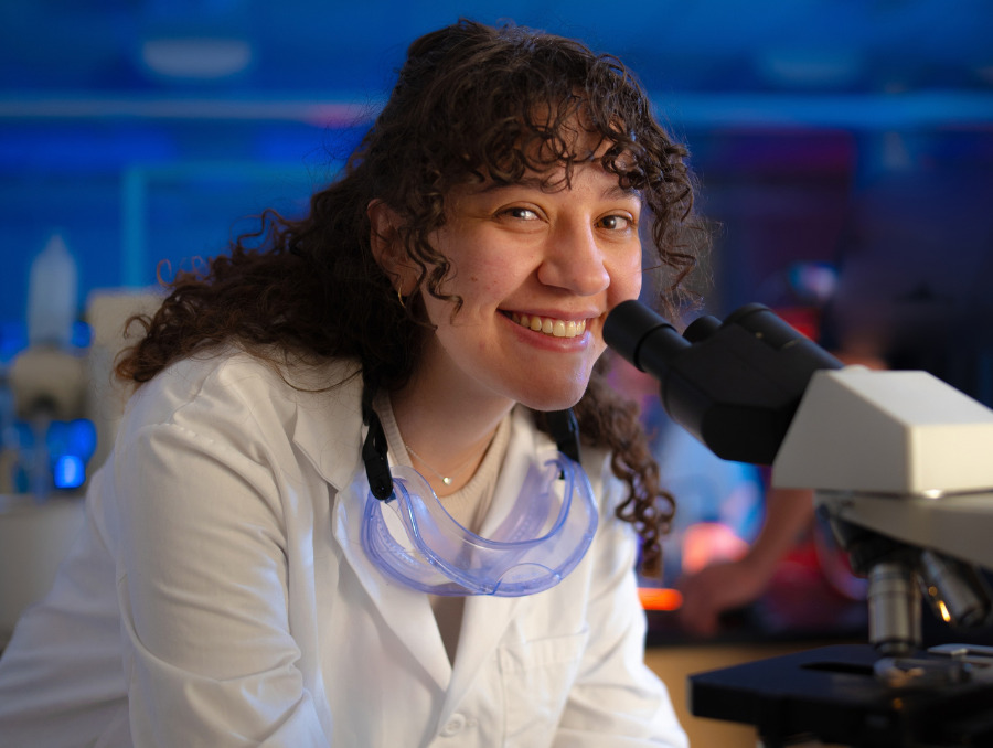 Tugba Selvi smiles next to a microscpe.