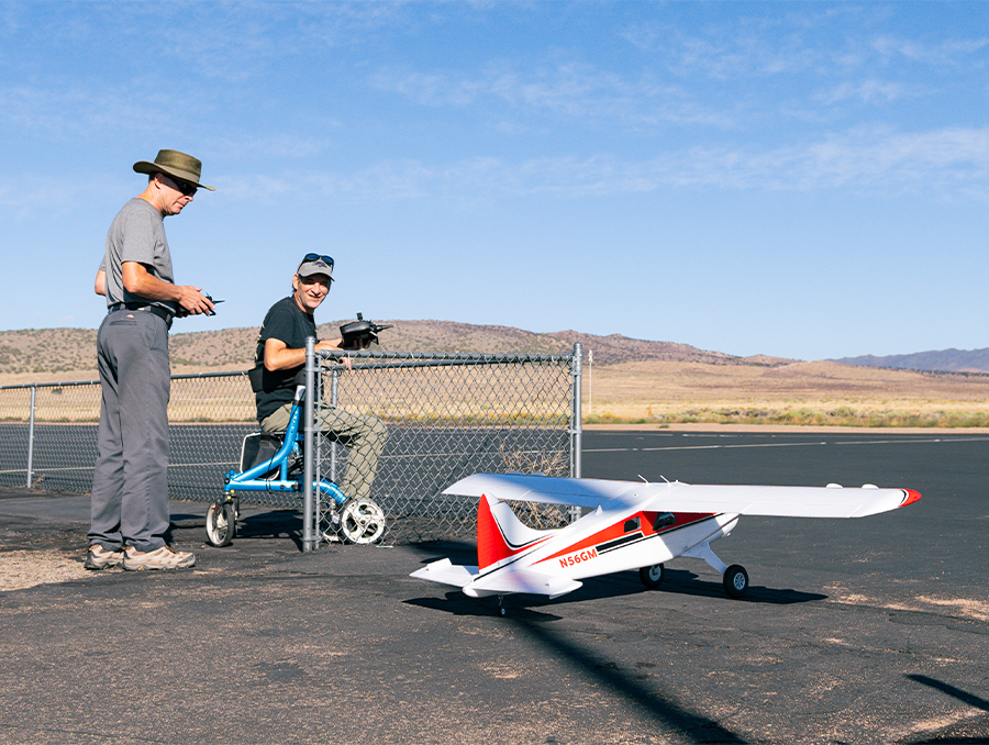 A person in a wheelchair next to a radio-controlled airplane.