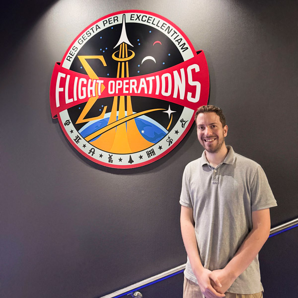 A man stands smiling in front of a badge on a wall that reads "Flight Operations"