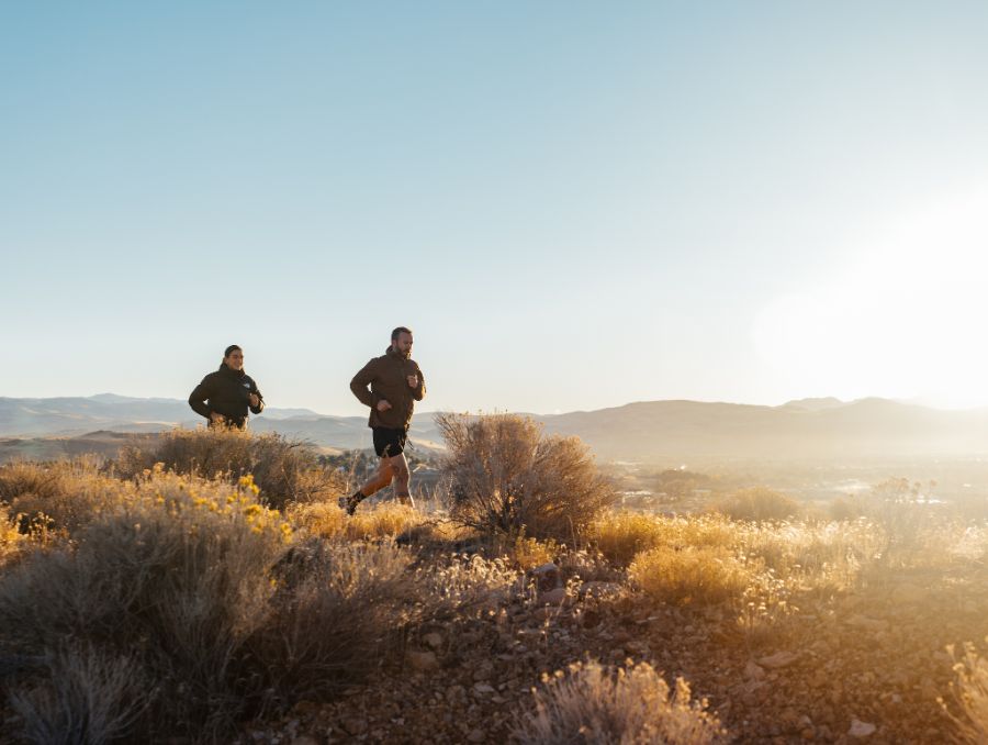 Two runners running through a field while the sun is beaming down.