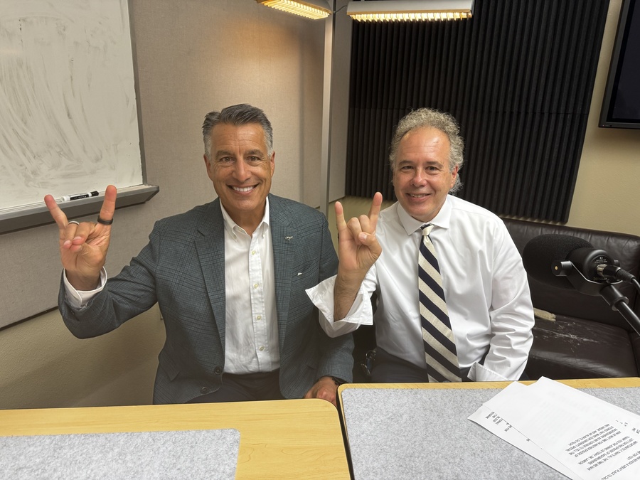 Daryl Lawson sits next to President Sandoval in the podcast recording studio, while making the Wolf Pack hand sign. 