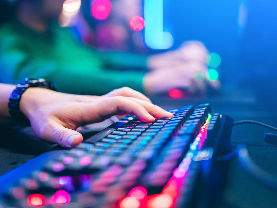 A person's hands on a keyboard that is lit with multicolor lights.