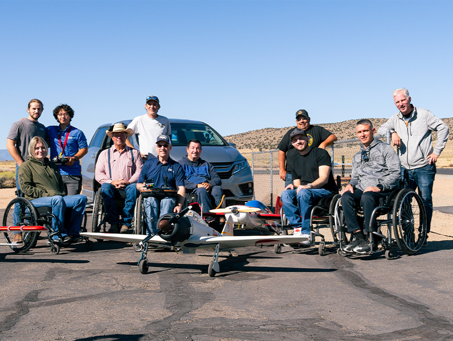 A group of people in wheelchairs posing with radio-controlled airplanes.